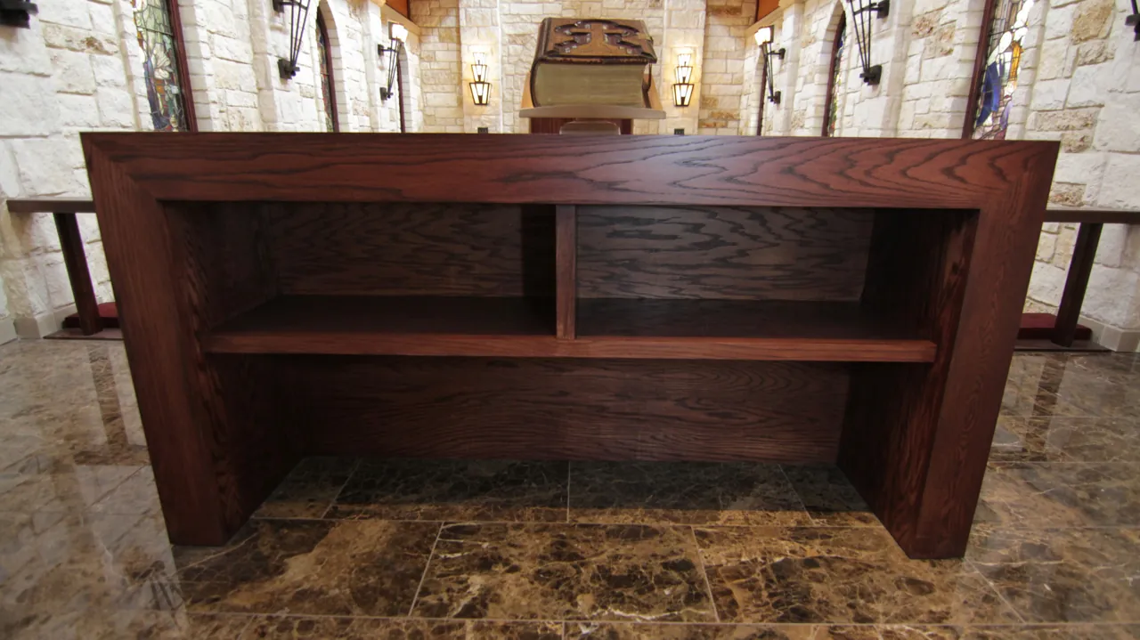 Open-shelf wood altar table on a marble floor in a limestone chapel