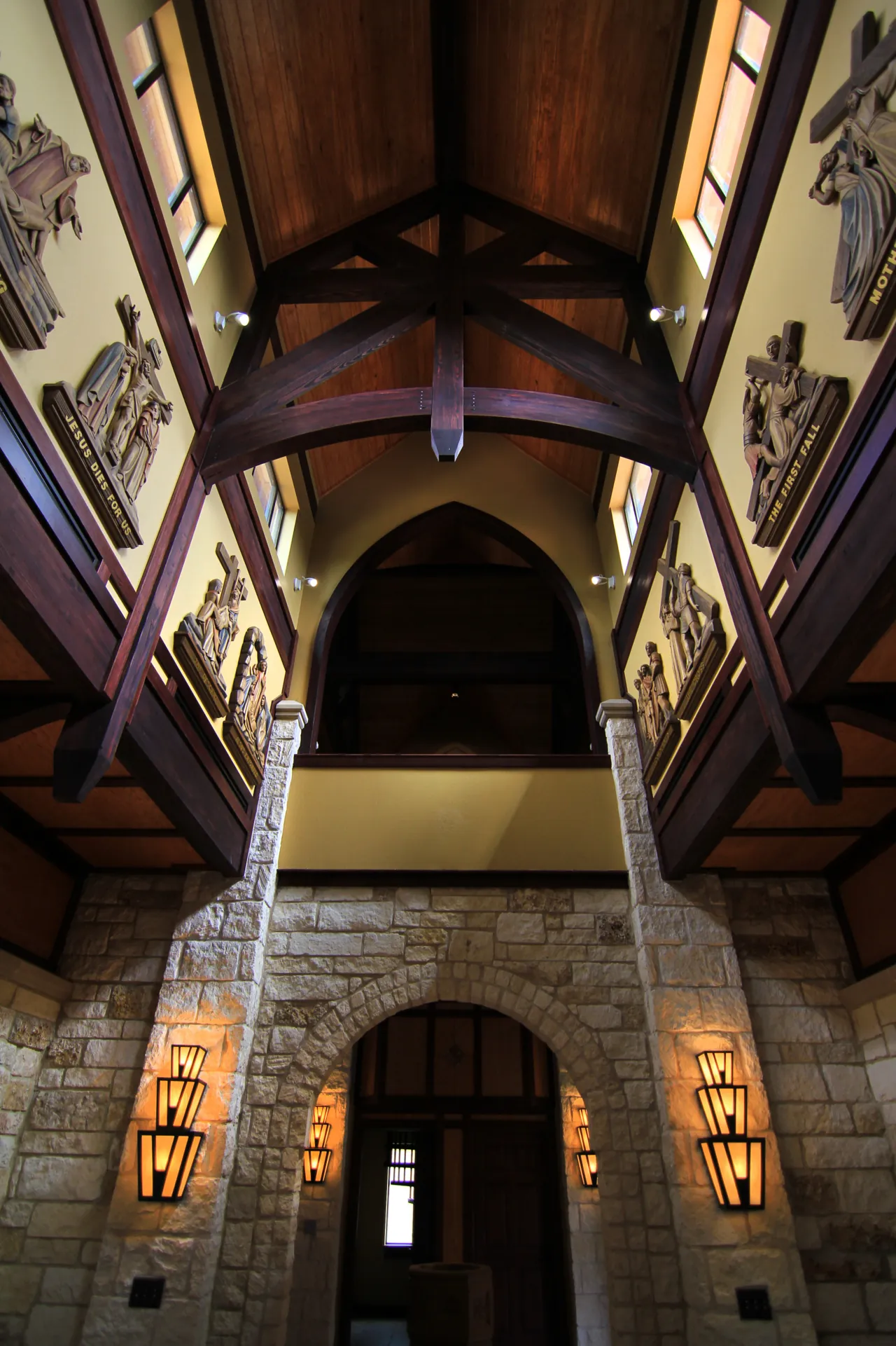 Tall limestone chapel nave with timber trusses, a pointed arch and wrought iron sconces