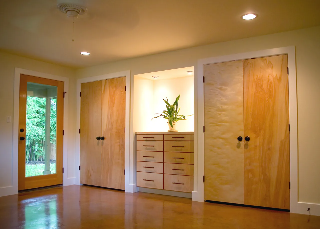 Wall of built-ins with figured veneer closet doors around a lit niche and drawer bank
