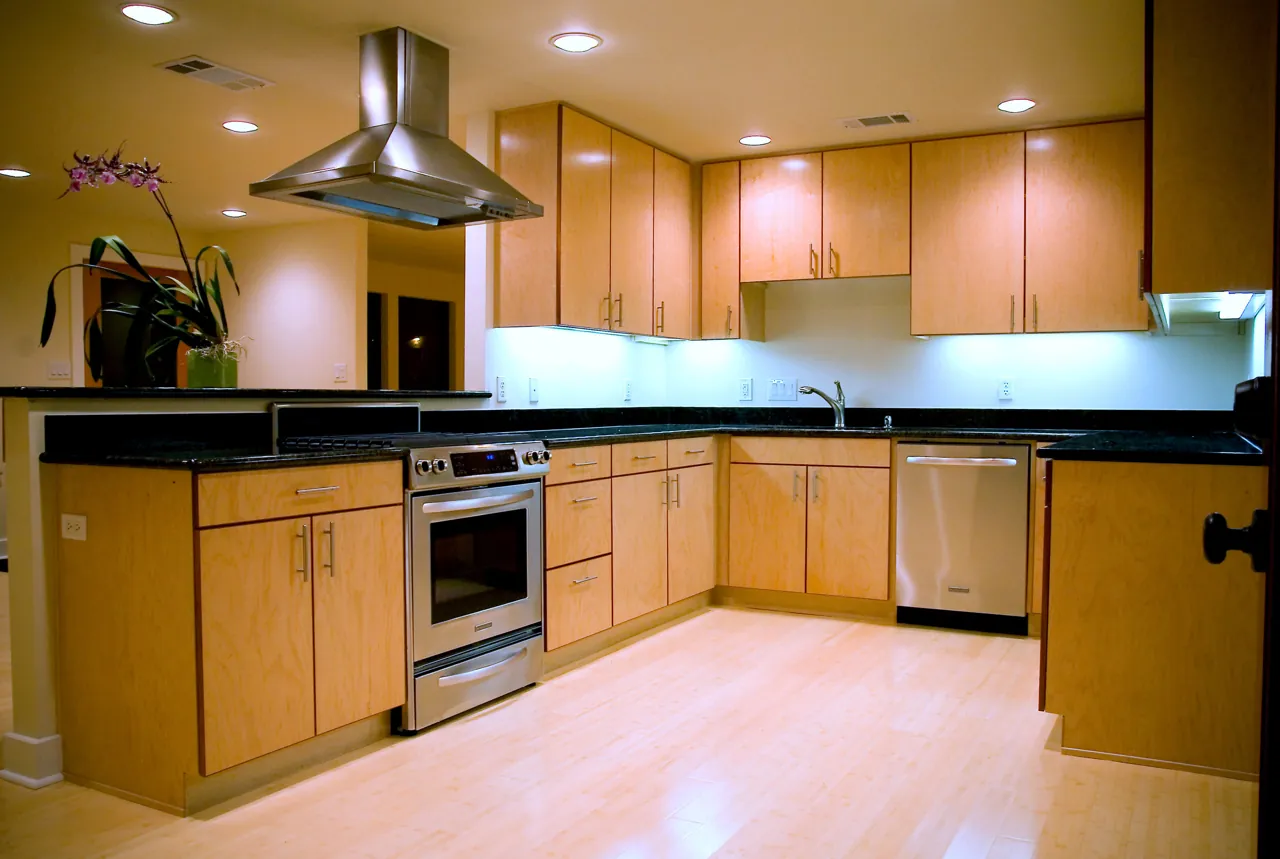 Flat-panel maple kitchen with dark stone counters, an island hood and under-cabinet lighting